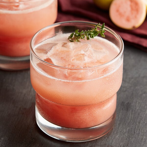 A glass of pink guava drink with ice and a sprig of thyme.