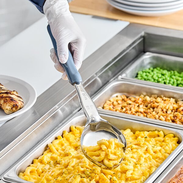 A hand in a glove holding a gray Vollrath Spoodle over macaroni and cheese.