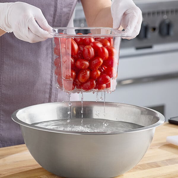 A woman using a Cambro clear plastic colander pan to drain cherry tomatoes.
