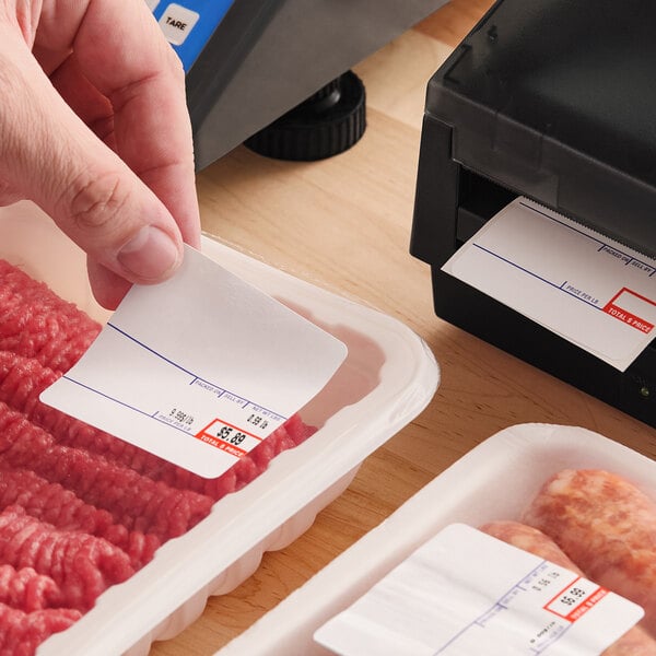 A roll of white pre-printed permanent direct thermal labels being applied to packaged meat products.