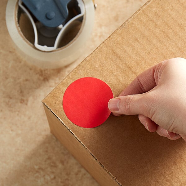 A hand using a Lavex red round sticker to label a box.