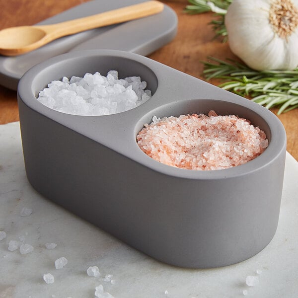 A Fox Run cement salt cellar with a wood spoon on a marble surface.