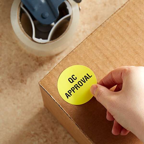 A hand holding a Lavex yellow paper label sticker and putting it on a cardboard box.