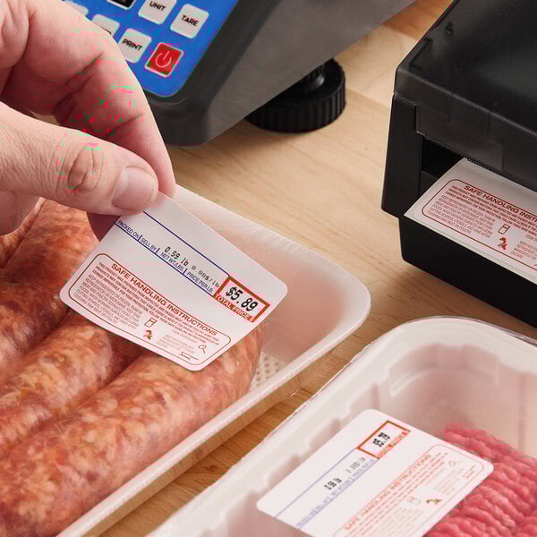 A roll of pre-printed permanent direct thermal labels for safe handling instructions, being applied to packaged meat products.