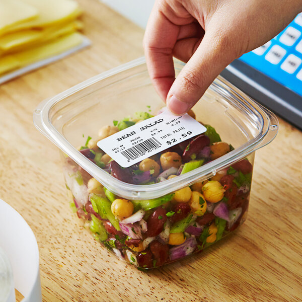 A hand holding a Globe E10 white blank label over a plastic container of food.