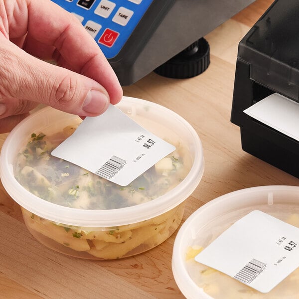A roll of white blank permanent direct thermal labels being applied to food containers.