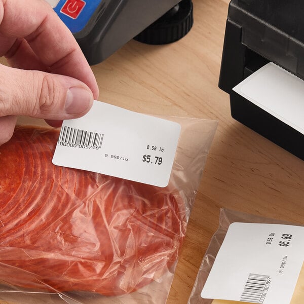 A roll of white blank permanent direct thermal labels being used to label packaged food products.