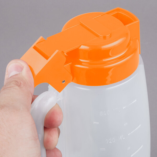 A person holding a Tablecraft dispenser jar with an orange lid.