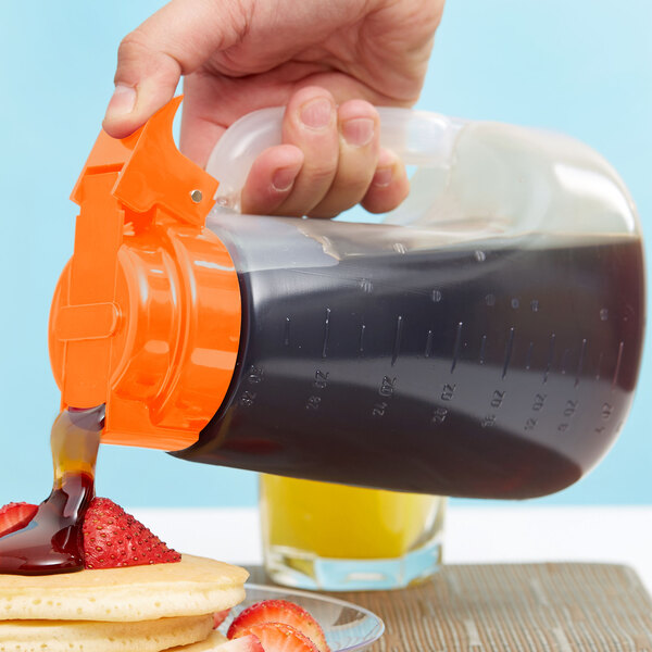 A person pouring syrup from a Tablecraft Dispenser Jar into a container.