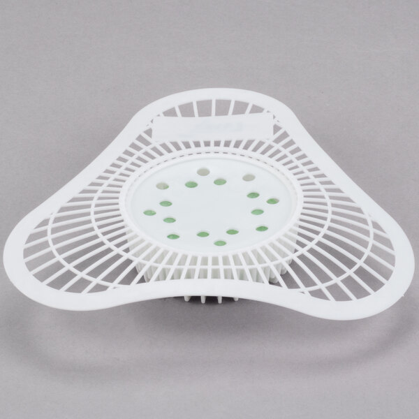 A white plastic urinal screen with holes and green dots.