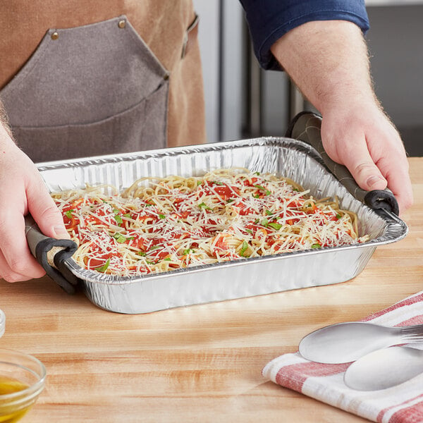 A hand holding a tray of spaghetti in a Choice half size heavy-duty foil steam table pan.