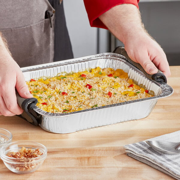 A hand using a Choice foil steam pan with food inside.