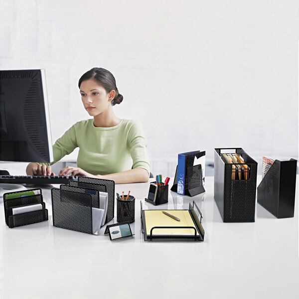 A woman sitting at a desk using a black punched metal pencil cup and cell phone stand.
