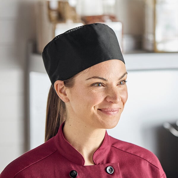 A woman wearing a black Uncommon Mesh Top Chef Skull Cap with a hook and loop closure on a professional kitchen counter.