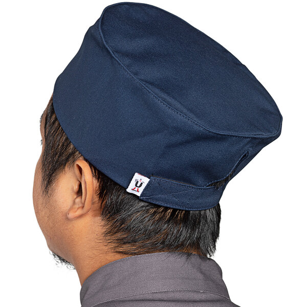 A man wearing a navy blue Uncommon Chef skull cap with a hook and loop closure.