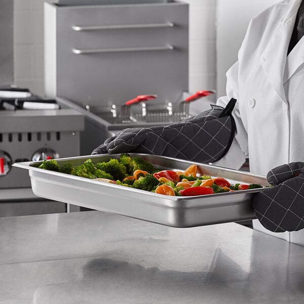 A chef holding a Carlisle stainless steel steam table pan with vegetables.