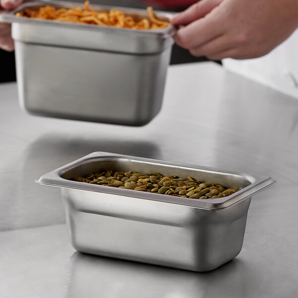 A person holding a container of food over a Carlisle stainless steel steam table pan on a counter.