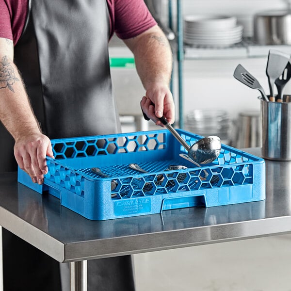 A man in an apron holding a blue Carlisle flatware rack with tools inside.