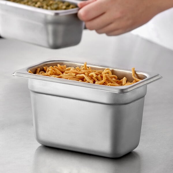 A person holding a Carlisle stainless steel steam table pan of food on a counter.