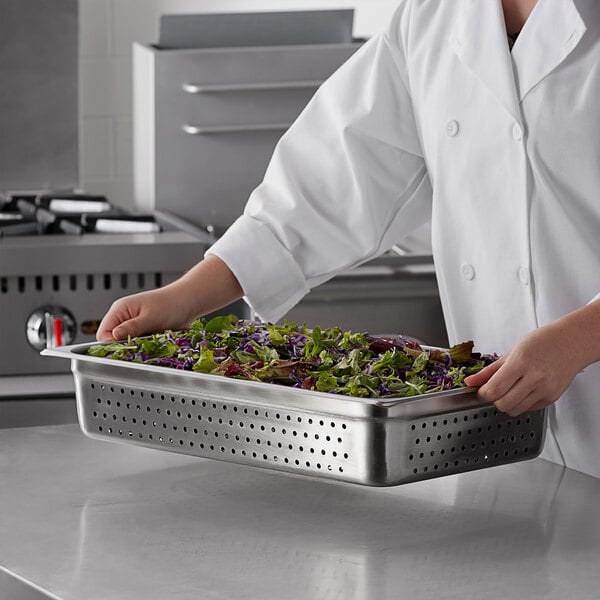A chef holding a Carlisle stainless steel perforated steam table pan filled with green and purple lettuce over a counter.