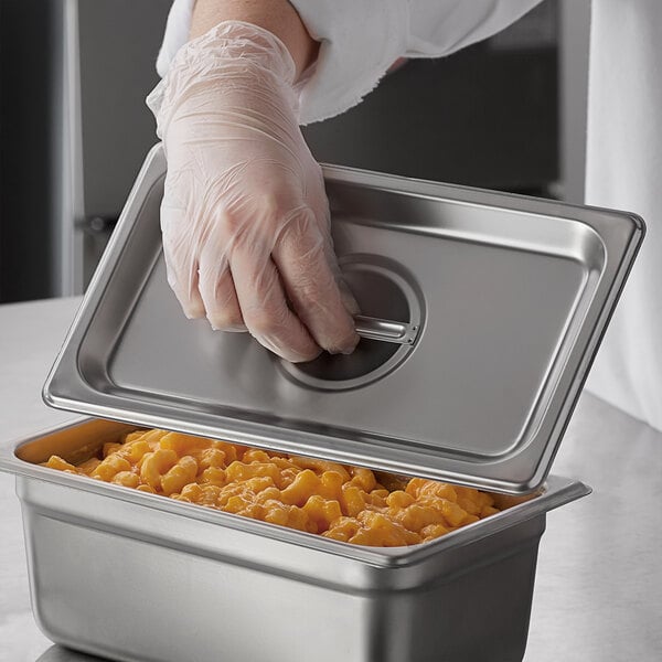 A person in gloves wearing gloves opens a stainless steel container of macaroni and cheese.