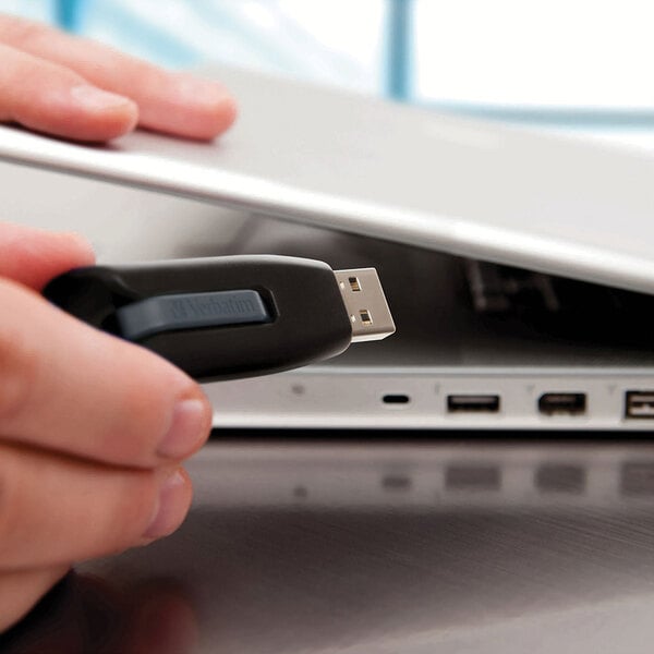 A person's hand holding a black and gray Verbatim Store 'n' Go V3 USB flash drive.