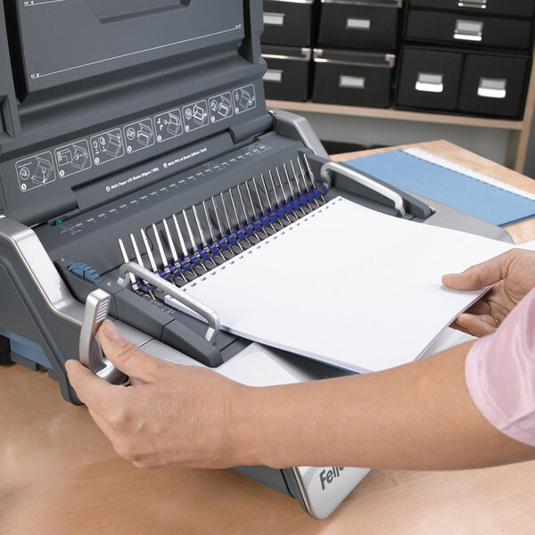 A person using a Fellowes electric comb binding machine to bind paper.