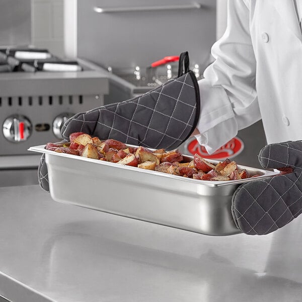 A chef holding a Carlisle stainless steel steam table pan of food.