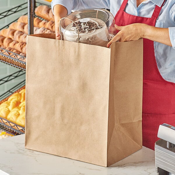 A woman in a red apron holding a Duro Grande natural kraft paper shopping bag full of food.