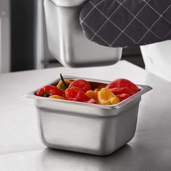 A Carlisle stainless steel steam table pan filled with peppers on a counter.