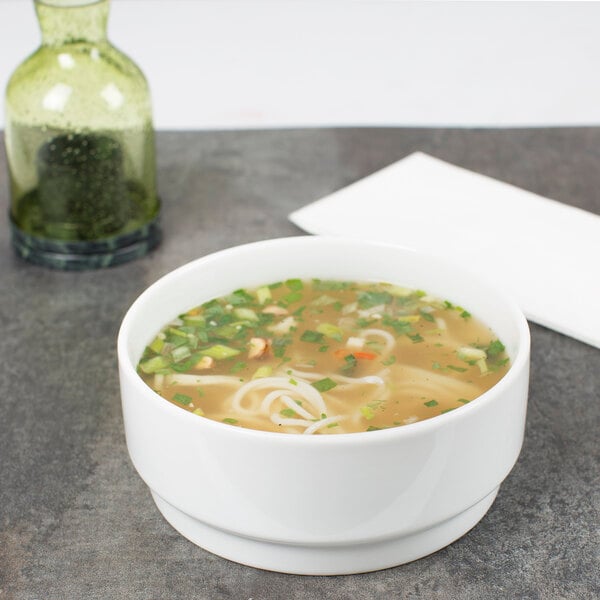 A stackable white porcelain bowl filled with soup, noodles, and vegetables.