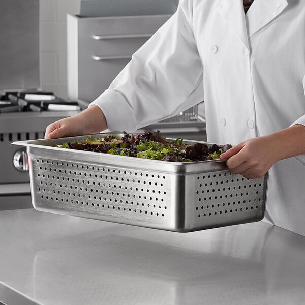 A chef holding a Carlisle stainless steel steam table pan full of salad.