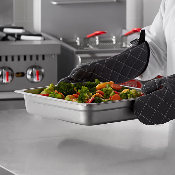 A chef holding a Carlisle stainless steel steam table pan full of vegetables.