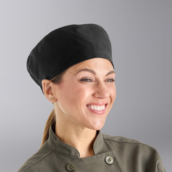 A woman wearing a black Uncommon Chef skull cap in a professional kitchen.