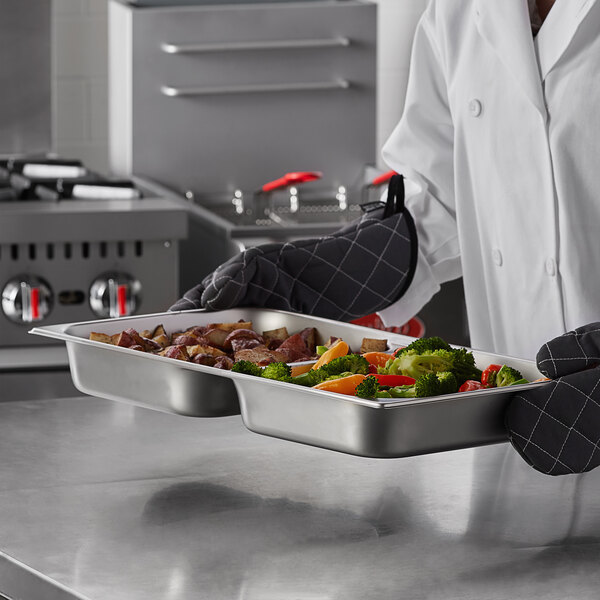 A chef holding a Carlisle stainless steel divided pan full of food.