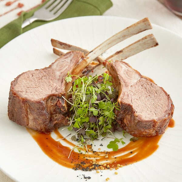 A plate with two lamb chops, a fork, and a side of greens on a table.