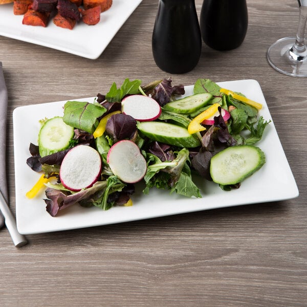 A white rectangular porcelain plate with a salad of radishes and carrots on a table.