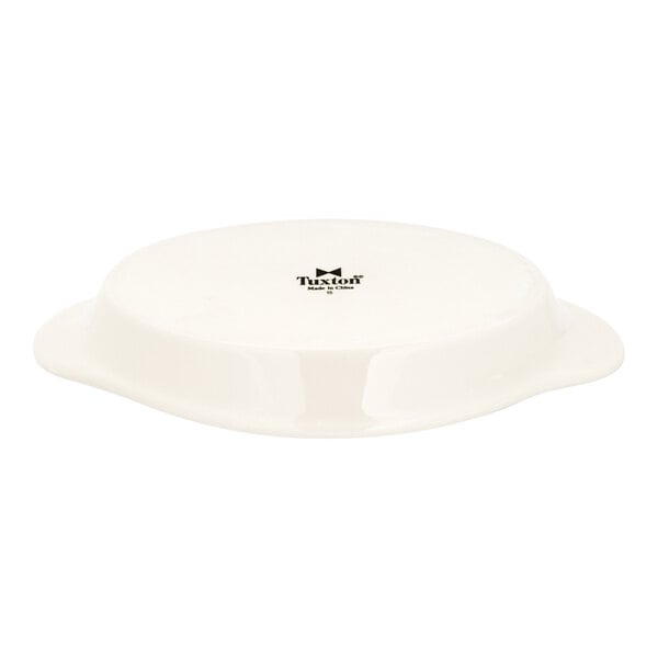 An eggshell-colored oval china dish with handles, shown upside down.
