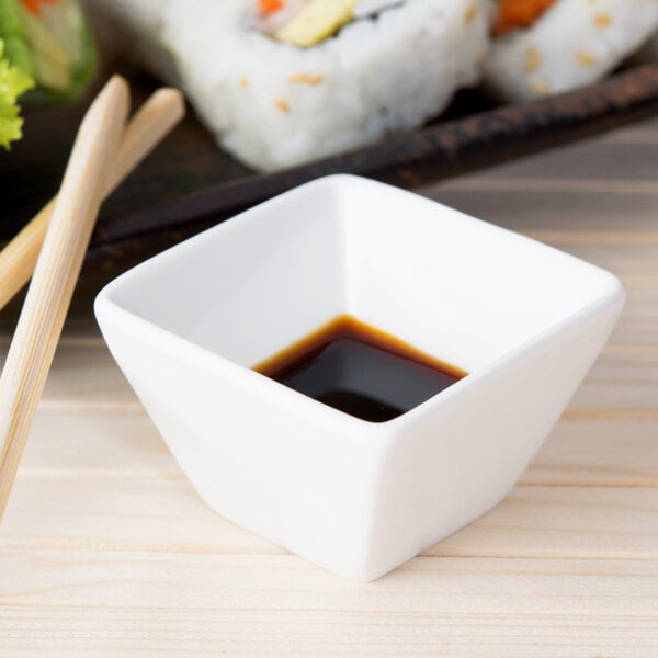 A white square American Metalcraft porcelain sauce cup with brown liquid inside on a white background.