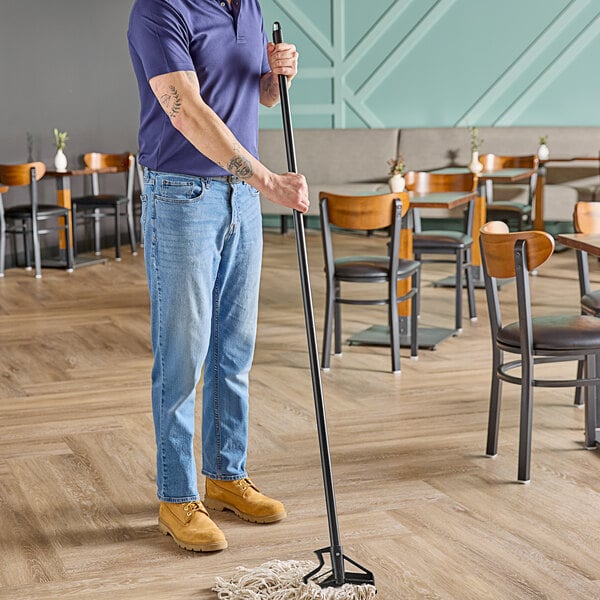 A man using a Carlisle Sparta vinyl-coated metal mop handle with a plastic head to mop the floor of a farm-to-table restaurant.