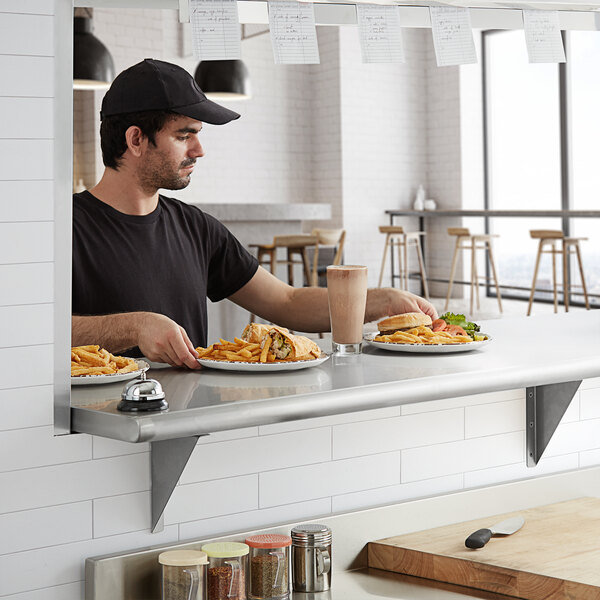 A man sitting at a counter with a plate of food on a Regency stainless steel shelf.