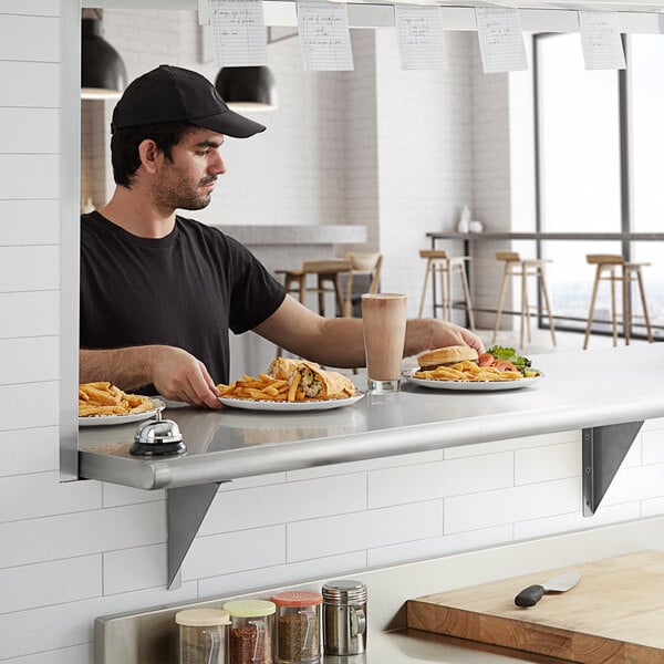 A man sitting at a table with a plate of food on a Regency stainless steel pass-through shelf.