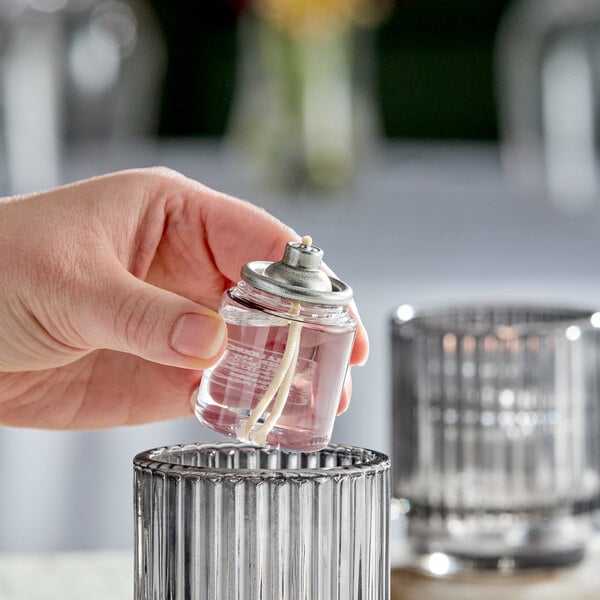 A clear liquid candle fuel cartridge with a metal top and wick being placed into a ribbed glass holder.