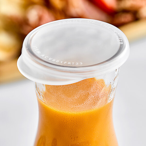 A Front of the House Drinkwise plastic lid on a 10 oz. carafe on a table with a glass of orange juice.