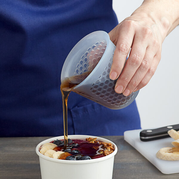 A person using an OXO Mini Squeeze & Pour measuring cup to pour brown liquid over a bowl of fruit.