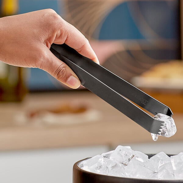 A person using matte black brushed stainless steel tongs to pick up ice.