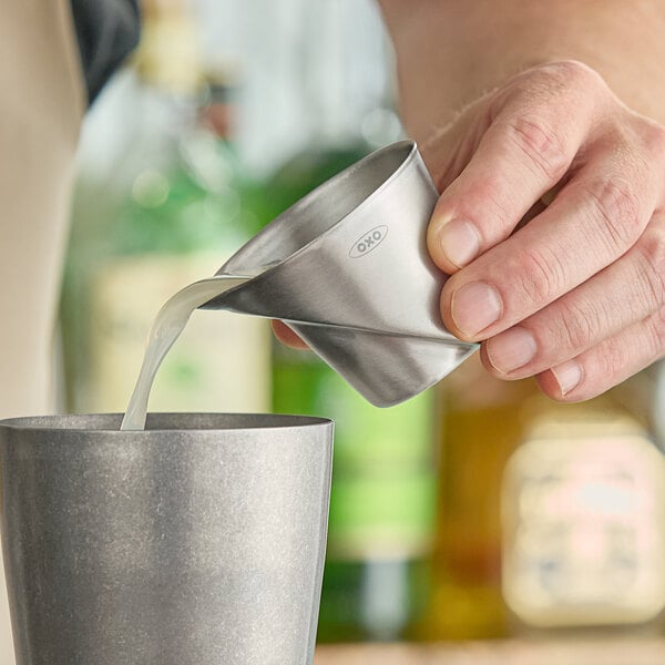 A person using an OXO stainless steel measuring cup to pour liquid into a cup.