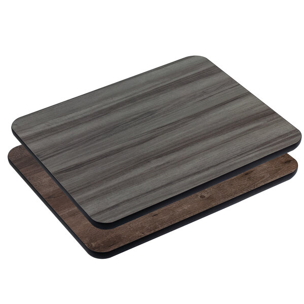 A close up of two American Tables & Seating wood table tops with a dark gray surface on one.