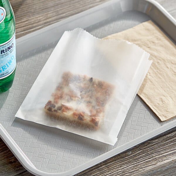 A tray with a sandwich wrapped in white wax paper, a piece of cake, and a bottle of water.