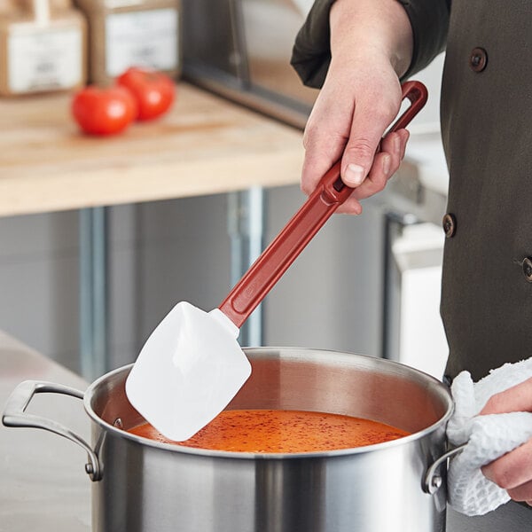 A person using a red Vollrath SoftSpoon to stir a pot of soup.